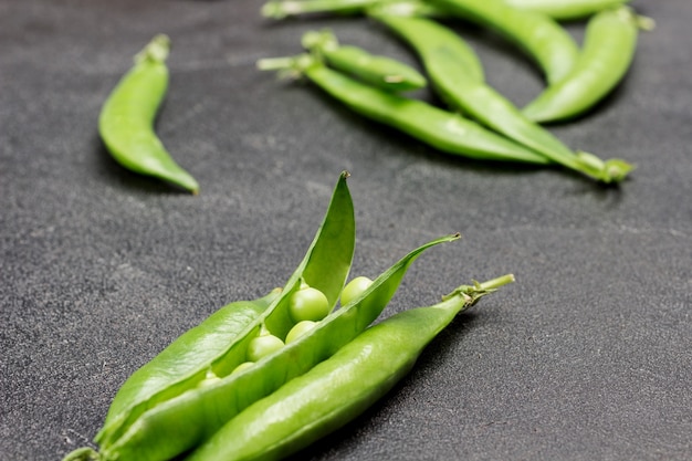 Opened pods of green peas and pods of green peas on table. Black background. Flat lay