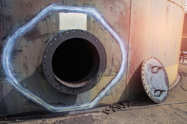 Opened rusty manhole on the black fuel tank  oil storage tank confined space