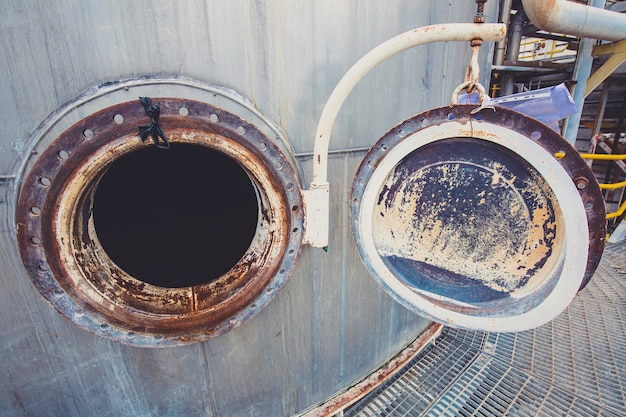 Opened rusty manhole on shell plate storage tank confined space