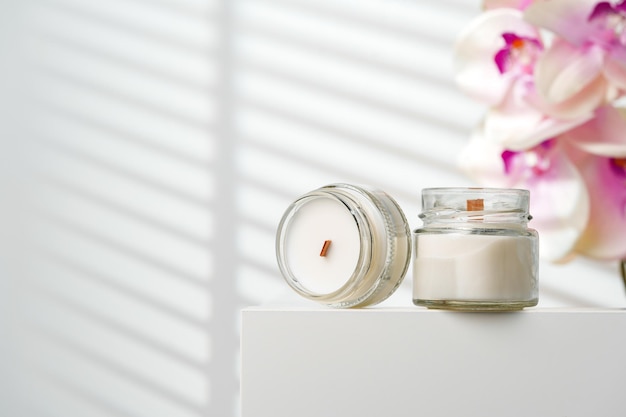 Opened scented candle jar on a white stand near a blurry orchid flower