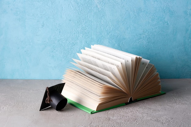 Opened textbook and student hat made of paper on a blue background copy space