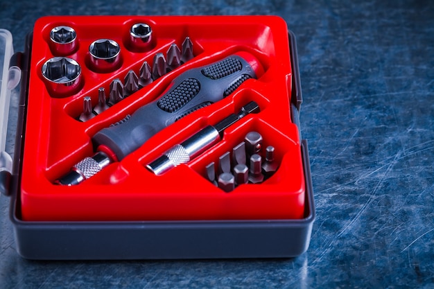 Opened tool case with screwdriver and replaceable bits and heads on scratched metallic construction concept.