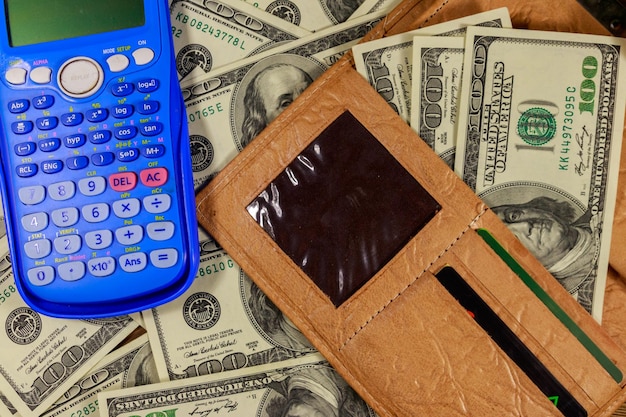 Открытый кошелек и калькулятор на фоне американских стодолларовых купюр