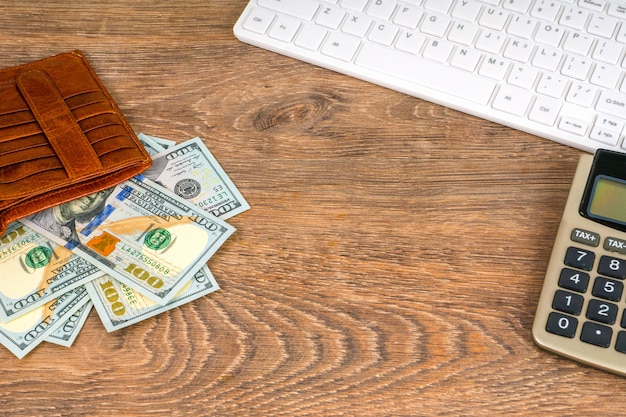 Opened wallet with dollar banknotes and calculator on table