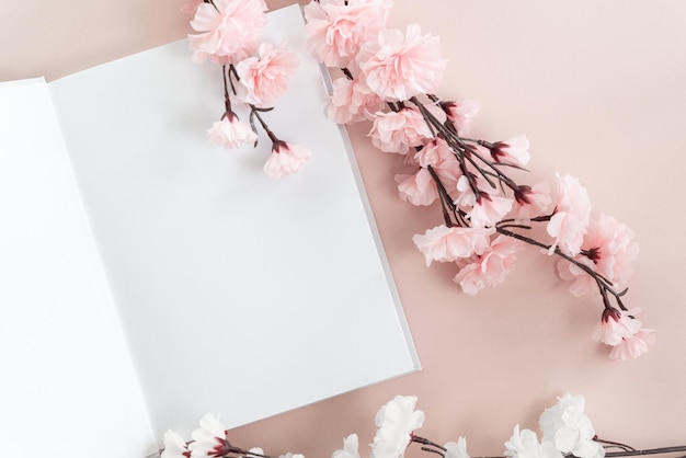 Opened white book mockup on a pastel pink background with white and pink cherry blossom.