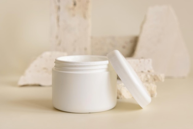 Photo opened white cream jar with a lid near biege stones close up cosmetic mockup