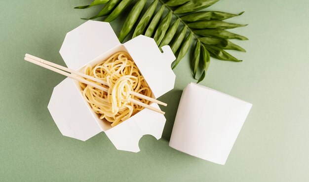 Foto scatola di carta wok aperta con tagliatelle e bacchette da mangiare modello di design vista superiore piatta su sfondo verde