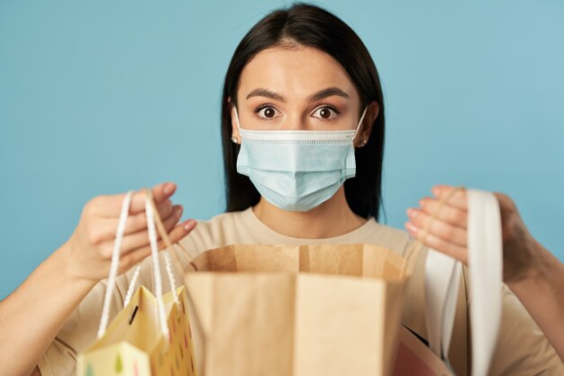 Openeyed lady posing in medical face mask and holding shopping bags in studio