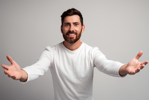 Openhartige gulle man met baard die open handen deelt en naar de camera kijkt met een vriendelijke glimlach, groet en regaling, blij je te zien. indoor studio-opname geïsoleerd op een witte achtergrond