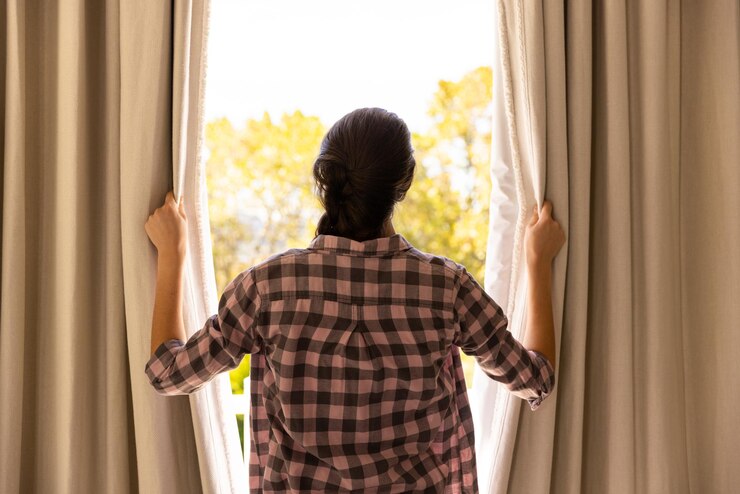 फोटो opening curtains woman in plaid shirt looking outside at sunny day