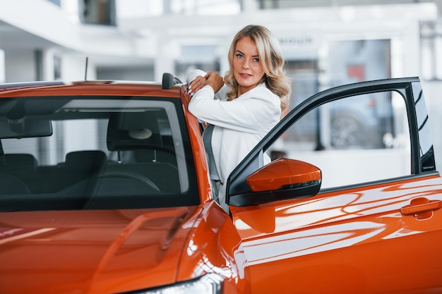 Opening the door Woman in formal clothes is indoors in the autosalon