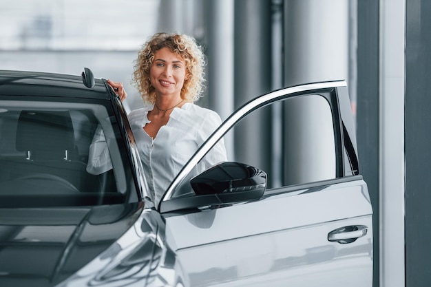 Opening the door Woman with curly blonde hair is in autosalon