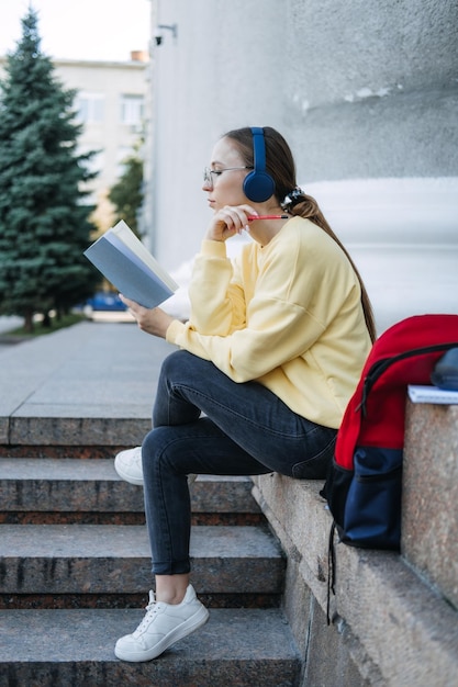 Openluchtportret van de gelukkige jonge vrouw van het studentenmeisje die aan audiolessen luistert