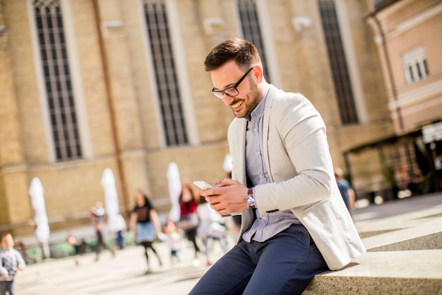 Openluchtportret van de moderne jonge mens met mobiele telefoonzitting bij zonnige dag