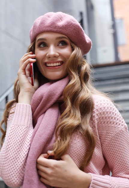 Openluchtportret van een jonge vrouw met een bril die een roze outfit draagt en een smartphone vasthoudt