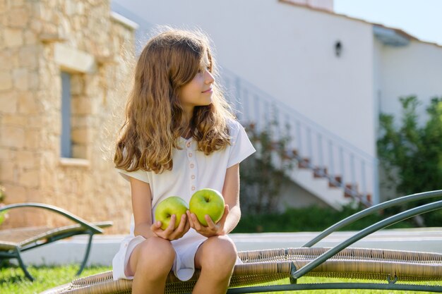 Openluchtportret van een kindmeisje met twee groene appels die in een tuinstoel zitten