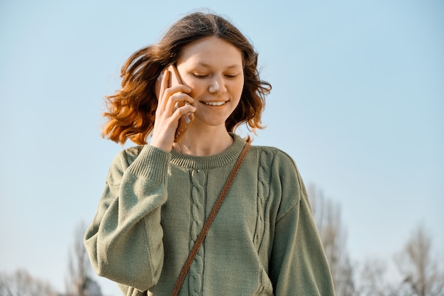 Openluchtportret van glimlachend tienermeisje dat op de telefoon spreekt