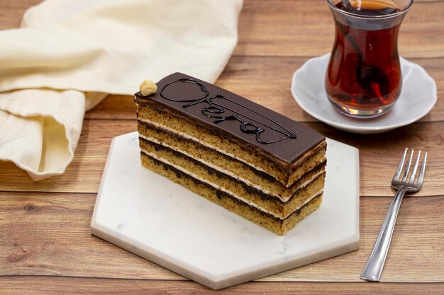 Opera cake on wooden background Cake with cream and chocolate filling along with a cup of tea