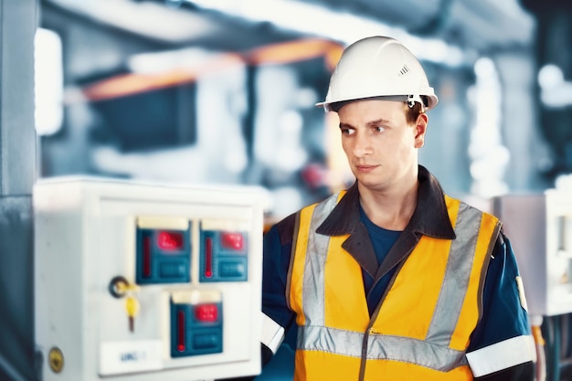 Operator or engineer in helmet and protective vest checks modern equipment in industrial plant