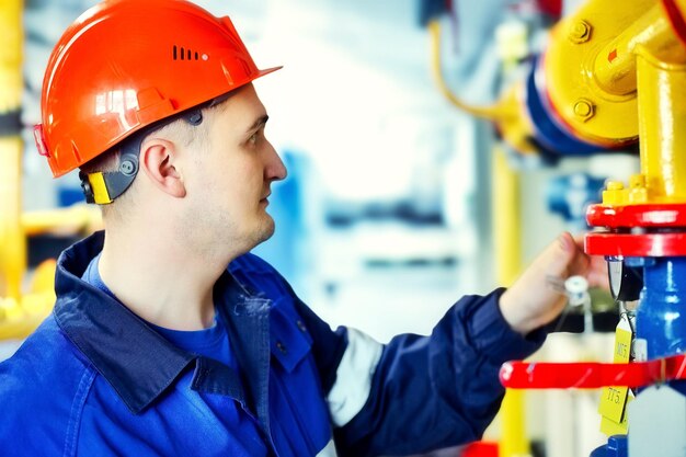 Operator of gas boiler house checks pressure on equipment Portrait of engineer in helmet at work Authentic scene workflow working man in boiler room Blurry background Gasification and energy