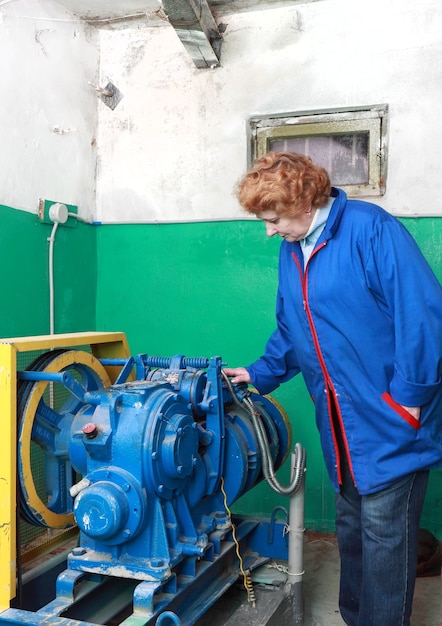 Operator woman-engineer in machine room (elevator) check the mechanical equipment.