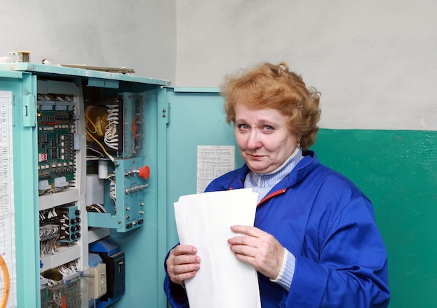 Operator woman-engineer in machine room (elevator) near electronic cabinet.