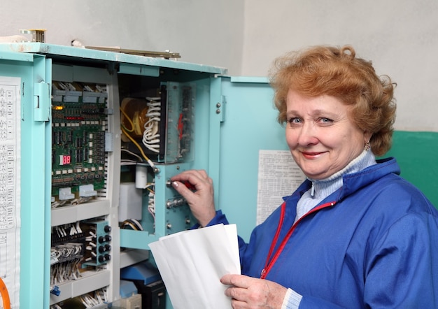 Operator woman-engineer in machine room (elevator) near electronic cabinet.