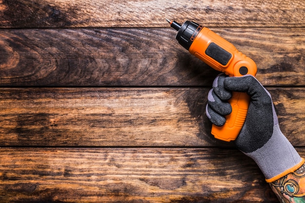 Foto opgeheven mening van de hand die van een persoon draadloze boor op houten achtergrond houdt