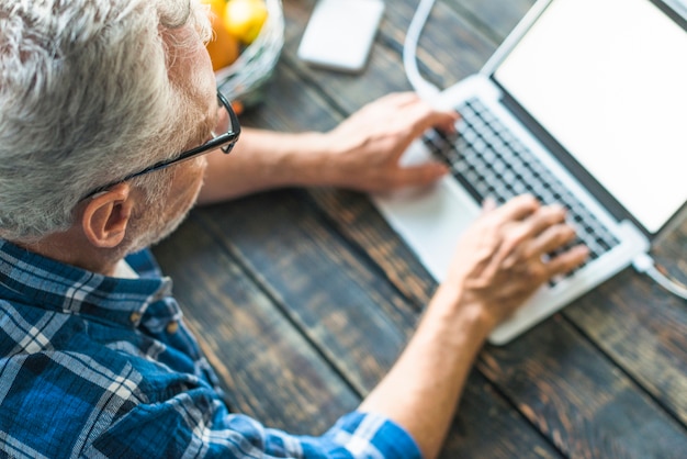 Foto opgeheven mening van het hogere mens typen op laptop over het houten bureau