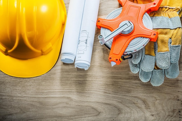 Opgerolde blauwdrukken beschermende handschoenen meetlint veiligheidshelm op houten bord