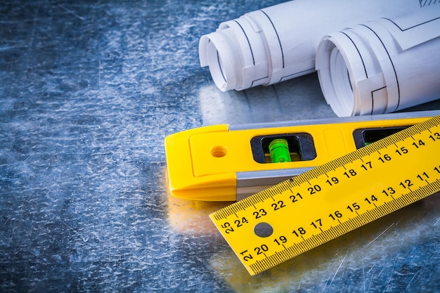 Opgerolde blauwdrukken liniaal en constructieniveau op metalen bekrast achtergrondonderhoudsconcept