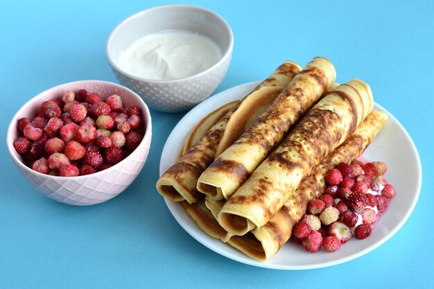 opgerolde blini op wit bord met wilde aardbei en zure room geïsoleerd, close-up