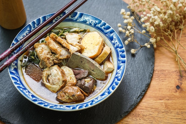 Opgerolde rijstnoedels in Fivespices-bouillon geserveerd in een betegeld kopje op een houten tafel