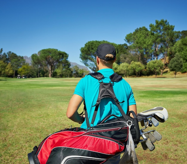 Opgesteld en klaar om golf te spelen Shot van een onherkenbare jonge man die met zijn golfuitrusting buiten op een golfbaan loopt