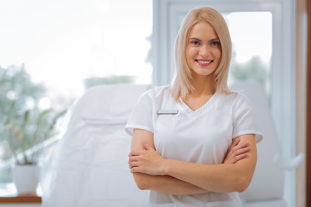 Opgetogen positieve vrouw die naar u glimlacht terwijl u als schoonheidsspecialist in de kliniek werkt