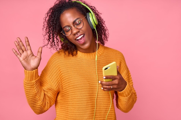 Opgetogen zwarte vrouw danst op ritme van melodie sluit ogen en luistert luid lied in koptelefoon