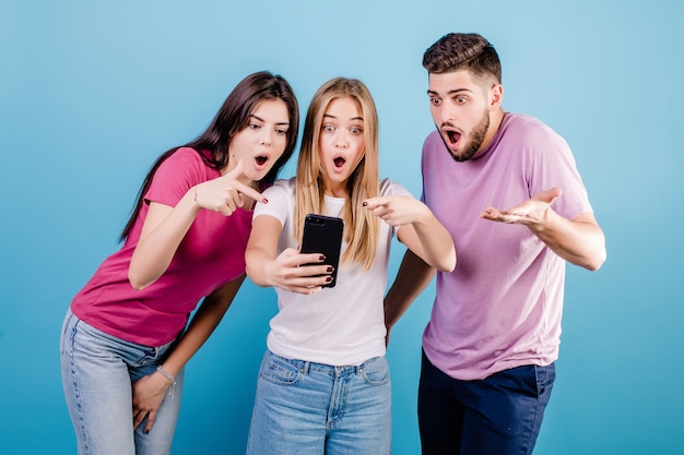 Opgewekte groep vrienden die op telefoon richten die op blauw wordt geïsoleerd