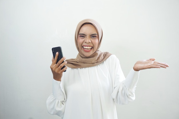 Opgewekte mooie Aziatische moslimvrouw die mobiele telefoon toont die over witte achtergrond wordt geïsoleerd