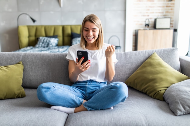 Opgewekte vrouw die media op inhoud online in een mobiele telefoonzitting op een laag in de woonkamer thuis letten