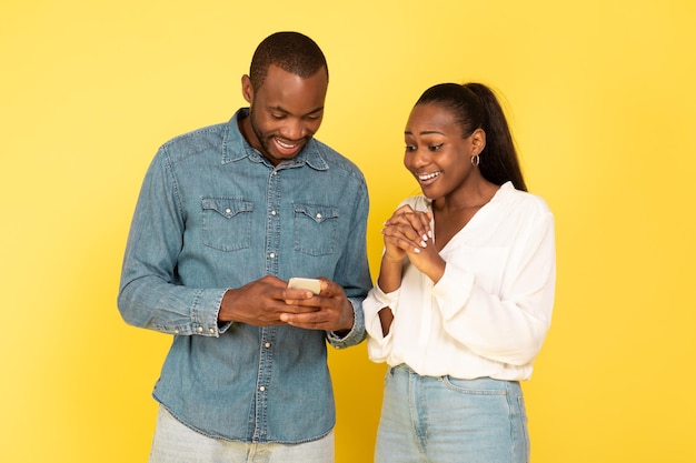 Opgewonden Afro-Amerikaans koppel dat samen telefoon gebruikt over gele achtergrond