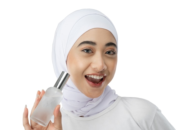 Opgewonden Aziatisch hijab-meisje in een witte jurk met een fles gezichtsverzorgingserum