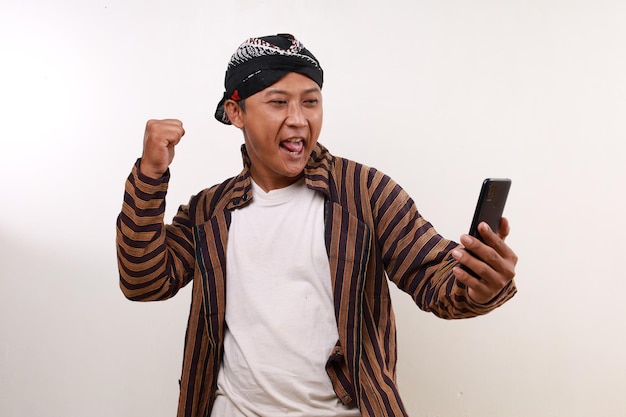 Opgewonden Aziatische man in Javanese kostuum met een mobiele telefoon terwijl hij zijn hand knijpt