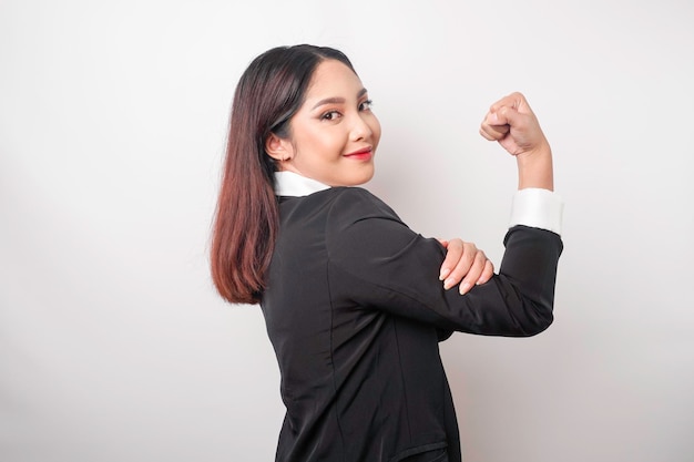 Opgewonden Aziatische zakenvrouw in een zwart pak die een sterk gebaar toont door haar armen en spieren trots op te tillen