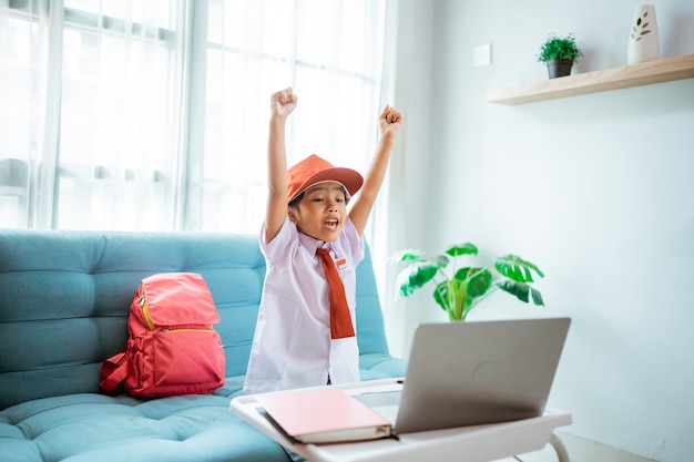 Opgewonden basisschoolleerling met uniform steekt haar arm op tijdens online les