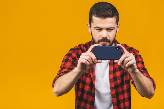 Opgewonden bebaarde man in geruite overhemd spelen op smartphone geïsoleerd over gele muur.