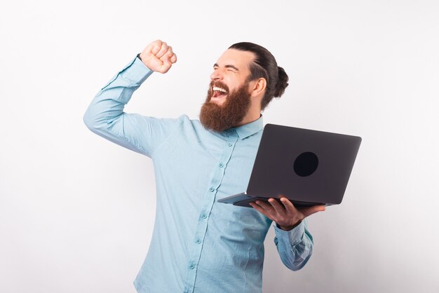 Opgewonden bebaarde man maakt het winnaarsgebaar en houdt een laptop vast.