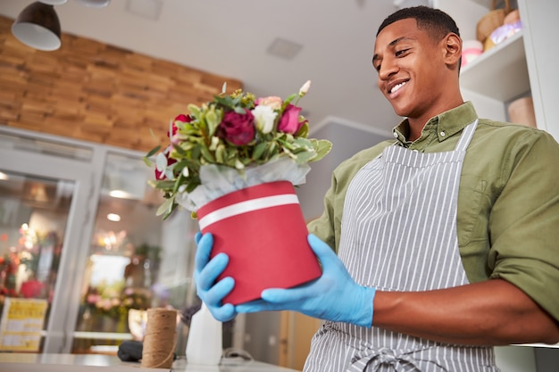 Opgewonden bloemenwinkelmanager met een pot in zijn handen kijkend naar een afgewerkt boeket met tevredenheid op zijn gezicht