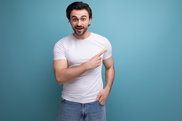 Opgewonden brunette man in witte t-shirt en spijkerbroek wijzende vinger