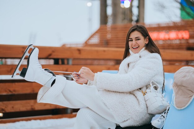 Foto opgewonden brunette meisje in witte broek witte bontjas die schaatsen aantrekt, gelukkige vakantie doorbrengt op de ijsbaan