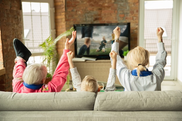 Opgewonden familie voetbal kijken, sportwedstrijd thuis. Oma, moeder en zoon juichen voor het nationale vrouwelijke voetbalteam met vertaling. Plezier hebben. Concept van emoties, ondersteuning, juichen.